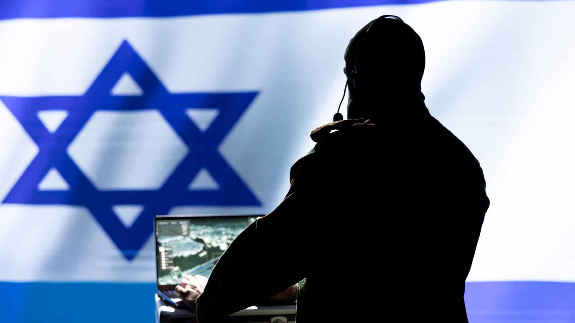 Homem com computador ligado em frente a bandeira de Israel