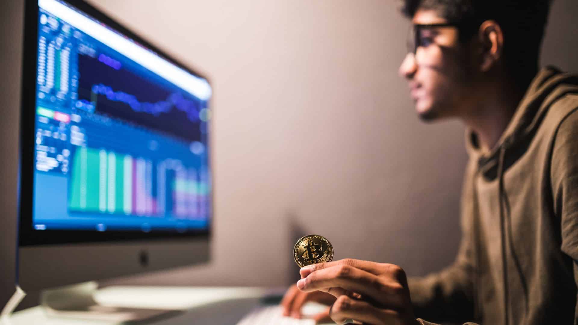 Investidor segurando bitcoin ao analisar graficos