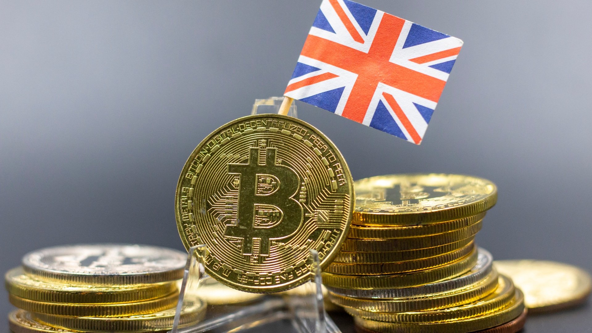 Reino Unido Impõe Multas Severas a Investidores de Cripto Por Falta de Dados Pessoais! 1 Bandeira do Reino Unido e pilha de Bitcoin