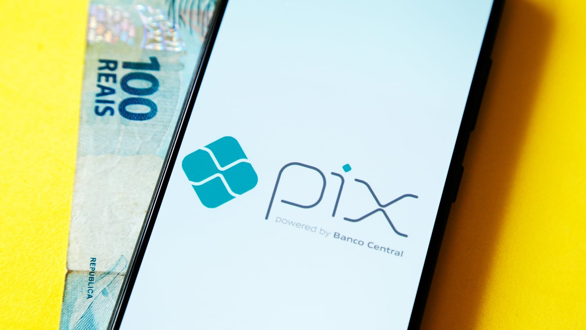Celular com tela do Pix e nota de 100 ao fundo