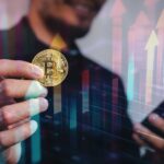 Homem segurando bitcoin com graficos