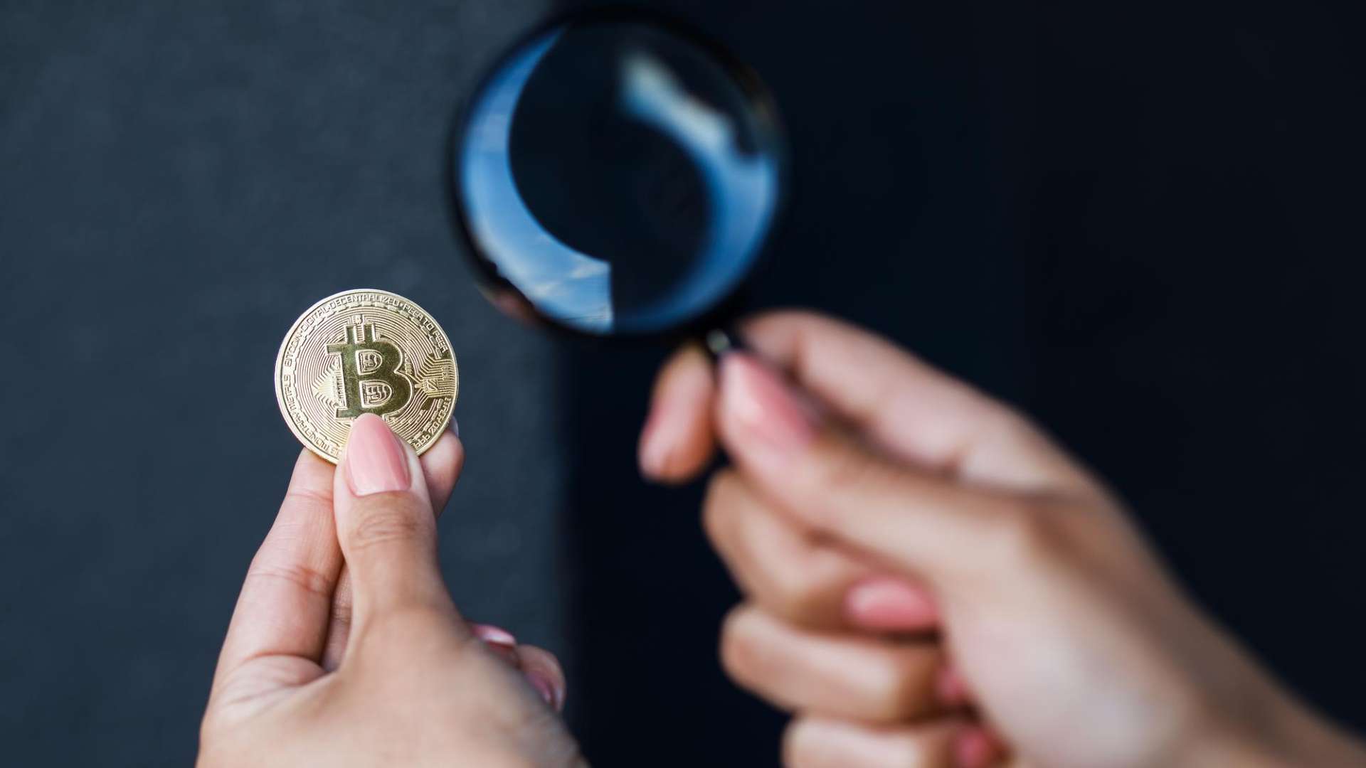 Pessoa segurando bitcoin e lupa em maos