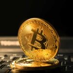 Bitcoin sobre computador apontando para baixo